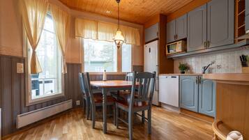 Una habitación con paneles de madera, una mesa de comedor con sillas, una zona de cocina con armarios y electrodomésticos, y una ventana con cortinas.