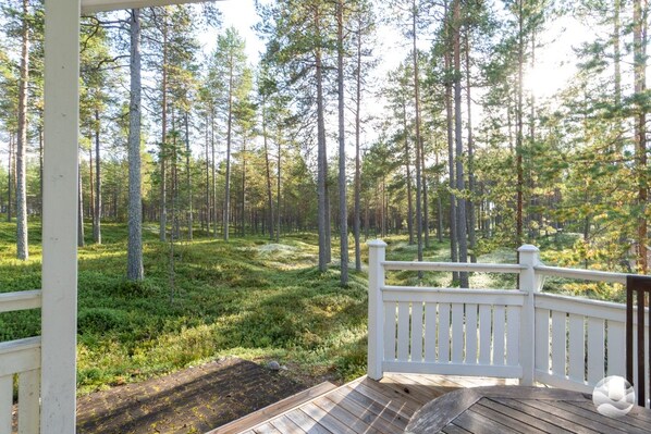 A wooden deck with a white railing overlooking a forested area.