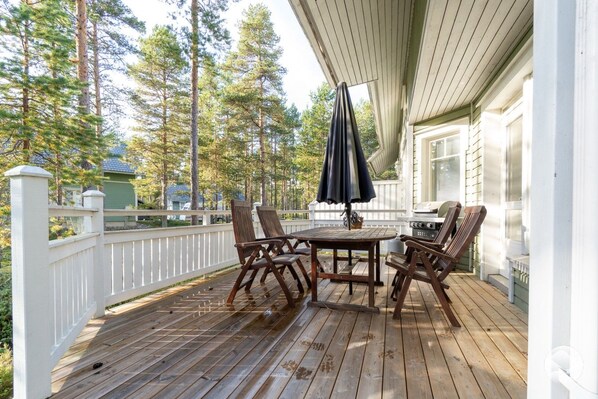A wooden deck with a table and chairs, a grill, and a white fence.