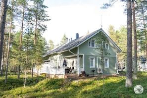 A two-story house with a porch, surrounded by a forest.