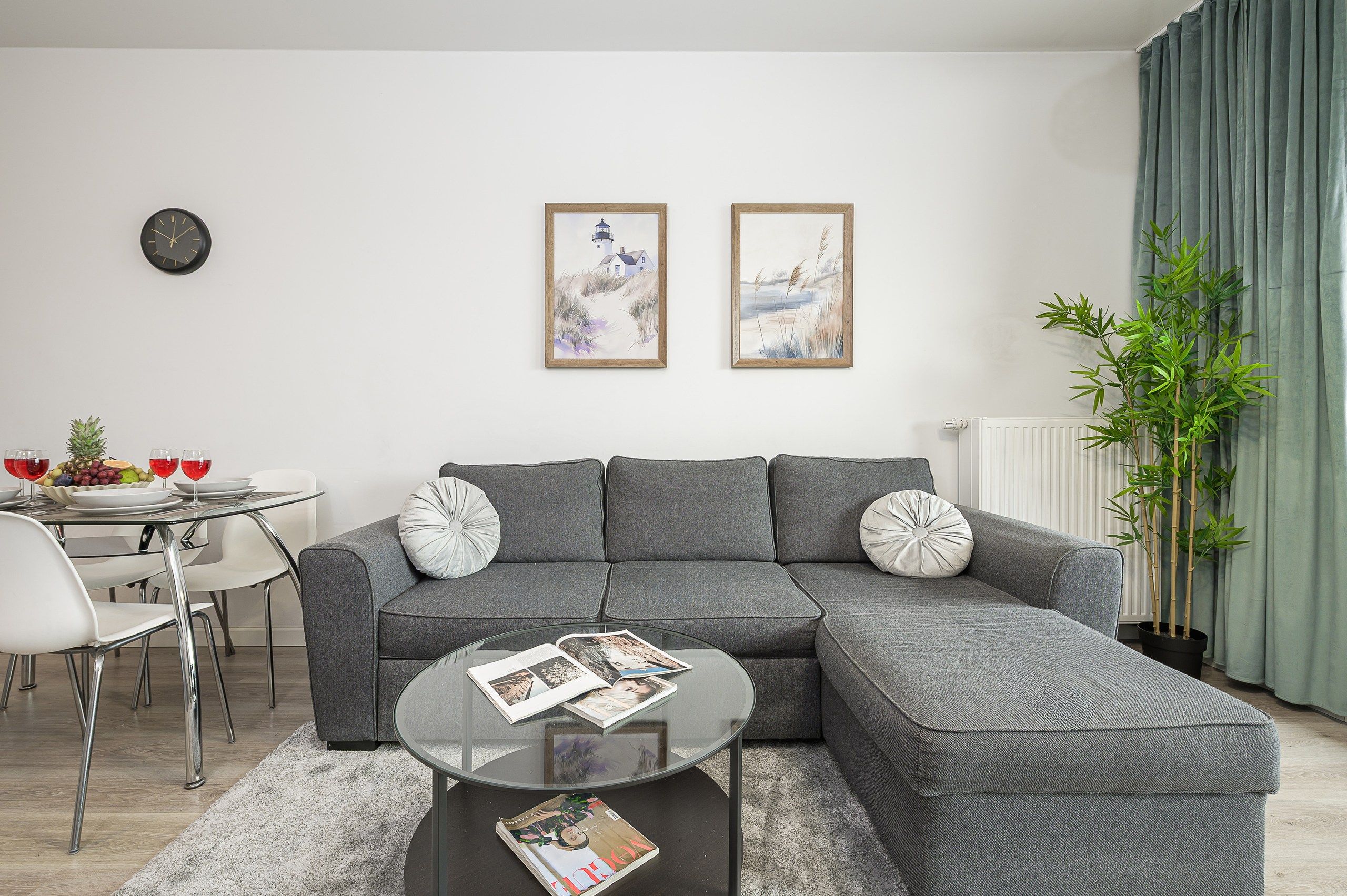 Una sala de estar moderna con un sofá seccional gris, una mesa de centro de vidrio y dos obras de arte enmarcadas en la pared.