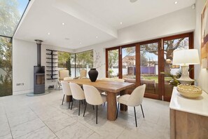 A modern dining area with a large wooden table, white chairs, a black vase, and a fireplace. - MUR1 - Modern 6-bed House in Wimbledon (London)