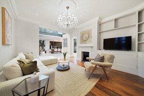 A modern living room with a chandelier, a fireplace, a television, and a sofa. - MUR1 - Modern 6-bed House in Wimbledon (London)