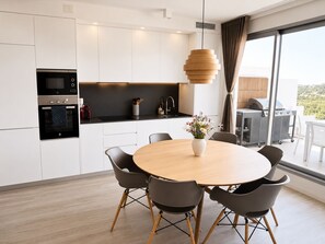 A modern kitchen with built-in appliances, a dining area with a round table and chairs, and a view of the outdoors through large windows. - RDR557- Penthouse w. Scenic Views | Sleeps 6 (Estepona)