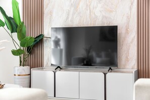 Un televisor de pantalla plana montado en un mueble blanco, con una pared de diseño marmolado al fondo.