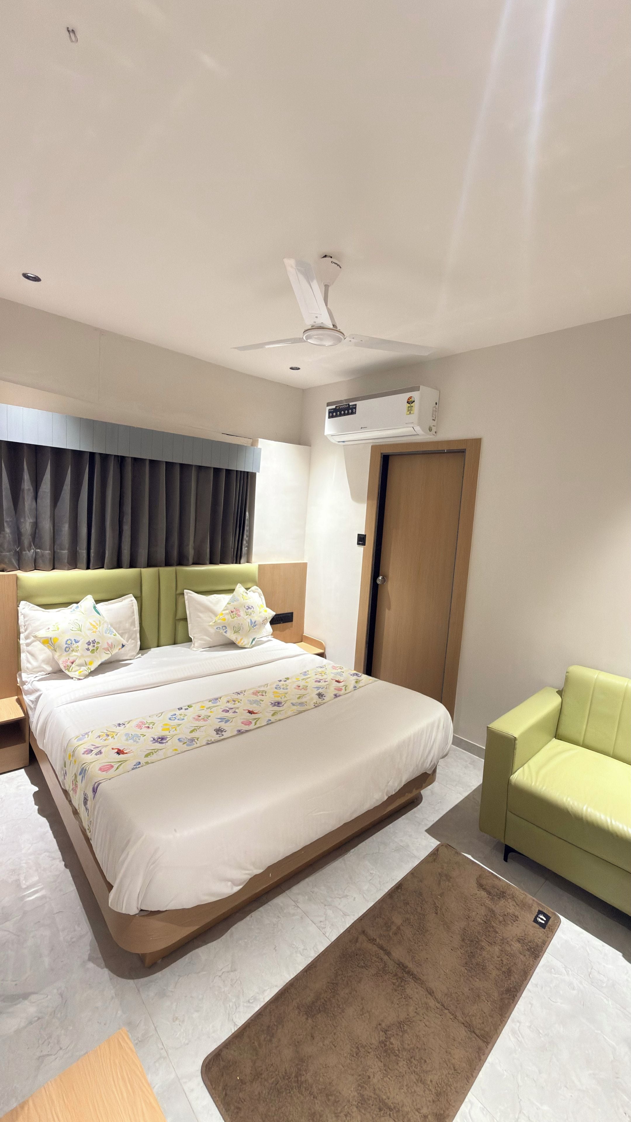 A modern hotel room with a large bed, a green sofa, a ceiling fan, and an air conditioning unit.