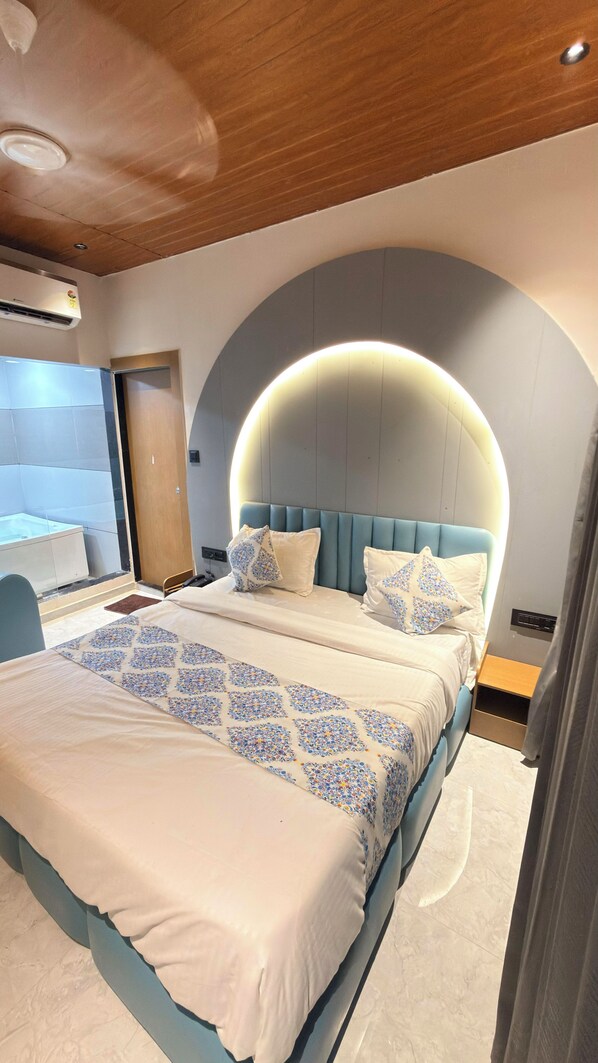 A modern bedroom with a large bed, a built-in bathtub, and a curved ceiling light.