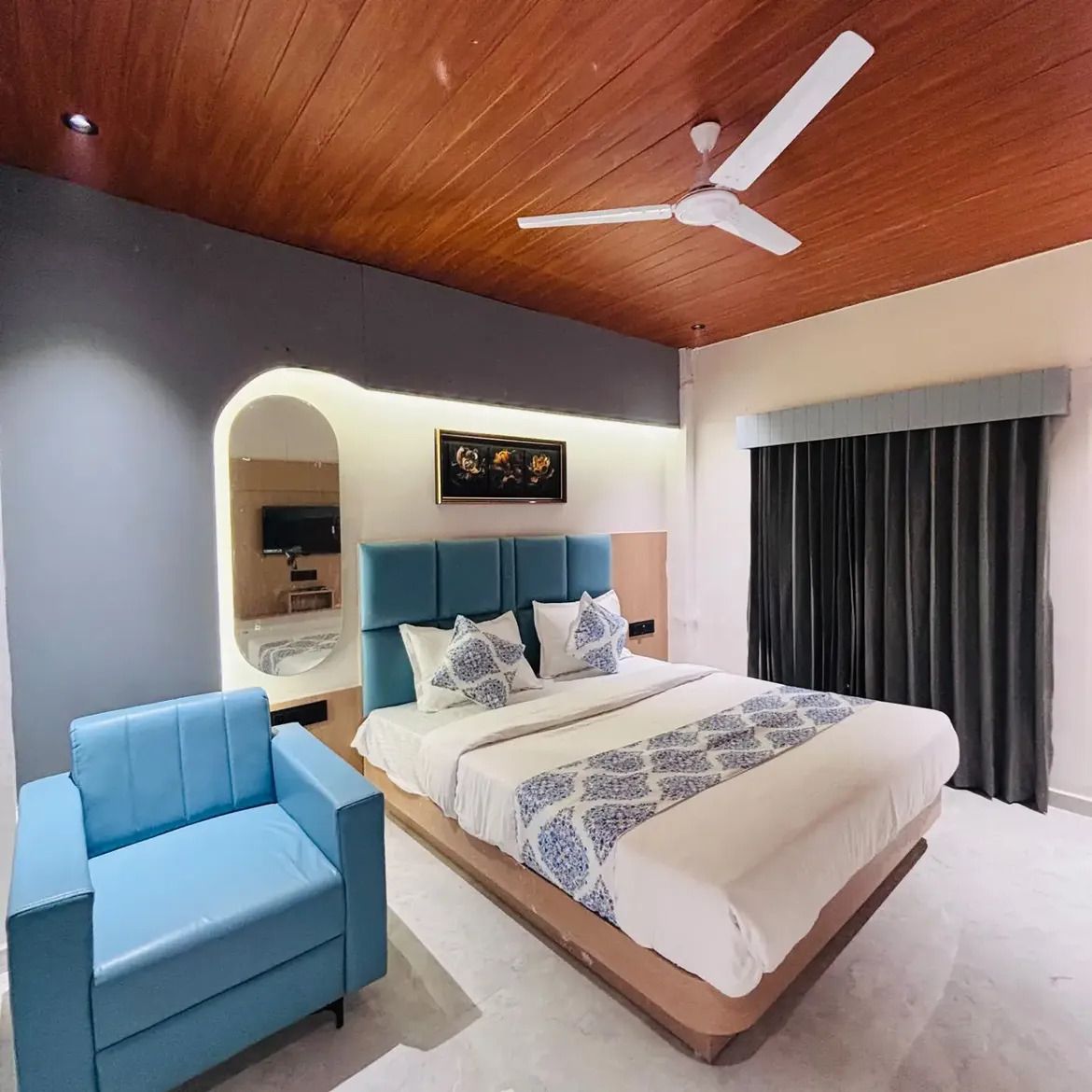 A modern bedroom with a bed, a blue armchair, a ceiling fan, and a large mirror.