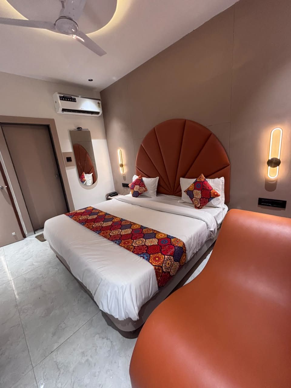 Una habitación de hotel con cama, ventilador de techo, aire acondicionado, espejo y lámpara de pared.