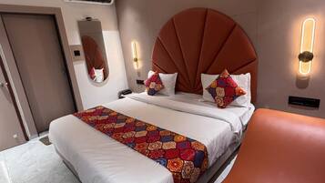 A hotel room with a bed, a ceiling fan, an air conditioning unit, a mirror, and a wall-mounted light fixture.