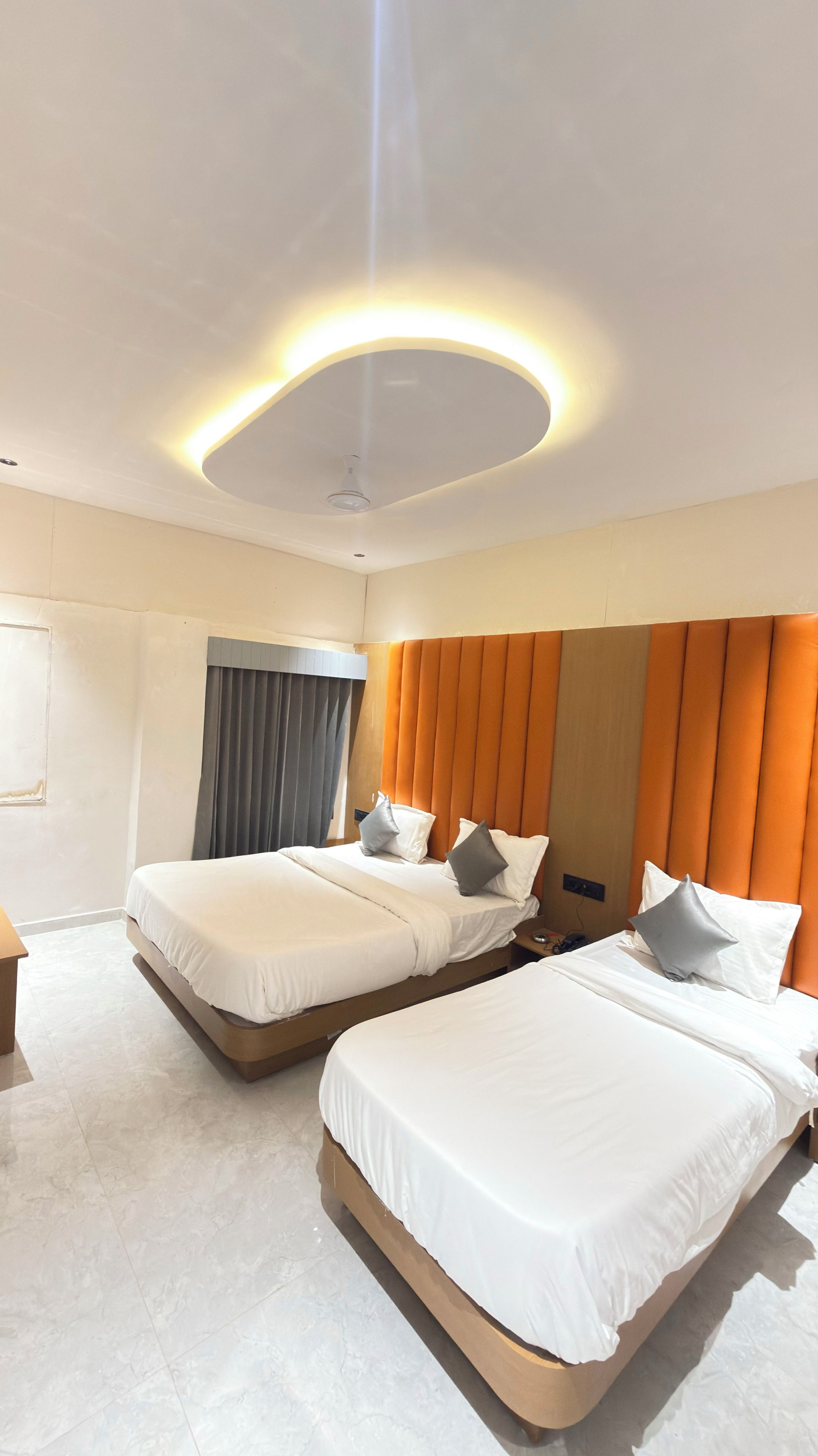 A hotel room with two beds, a modern ceiling light, and a large window with curtains.