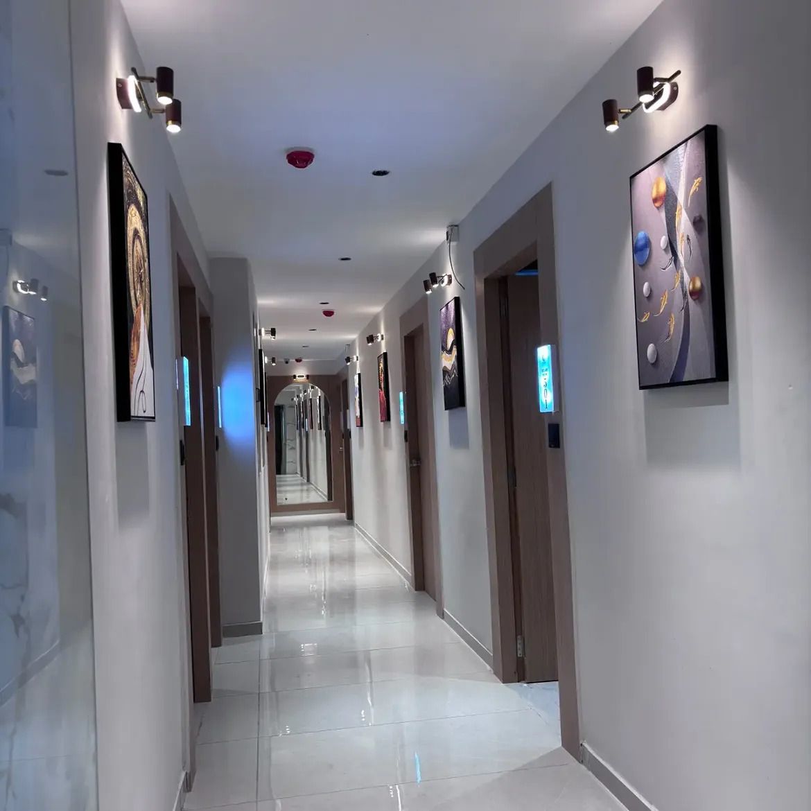 A hotel hallway with a long corridor, wall-mounted artwork, and ceiling lights.