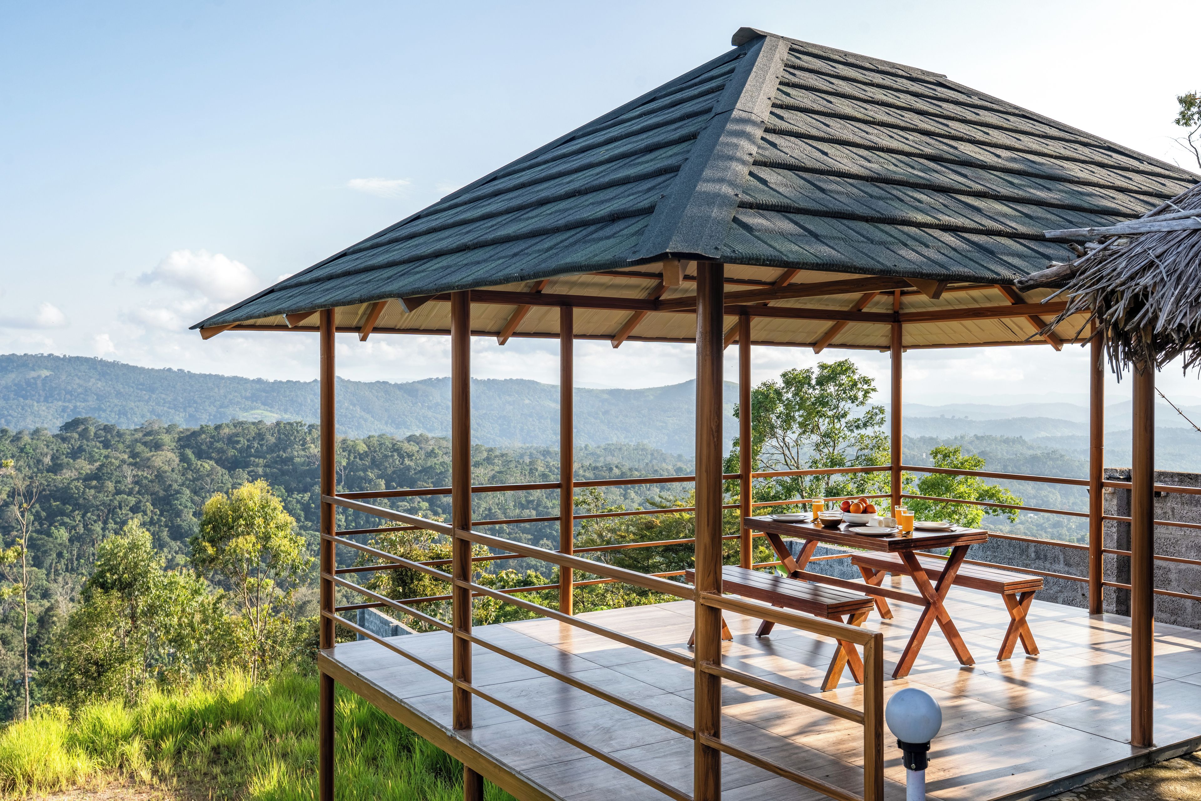 A wooden deck with a thatched roof pavilion overlooking a mountainous landscape.