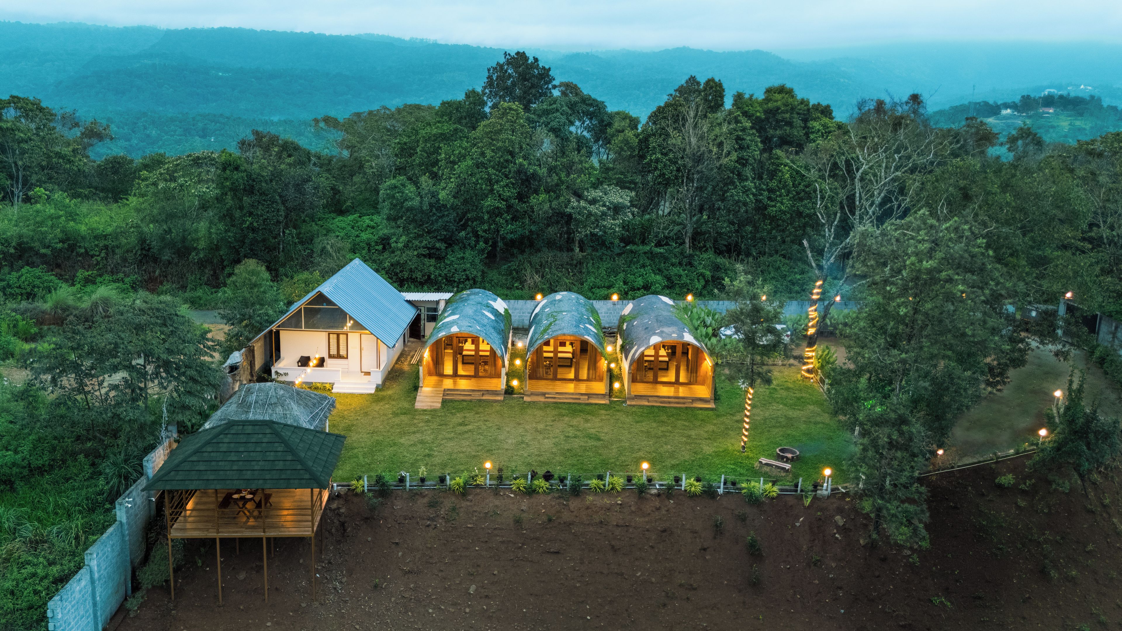 A secluded resort with multiple treehouse accommodations surrounded by lush greenery and a view of distant mountains.