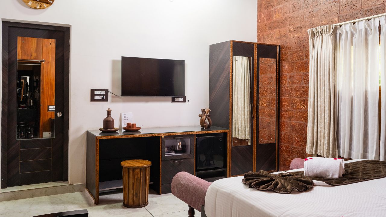 A hotel room with a bed, a desk with a television, a wardrobe, and a mirror.