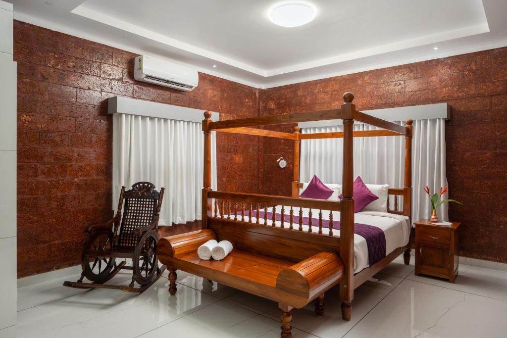 A four-poster bed with a wooden frame, a rocking chair, a bedside table, and a wall-mounted air conditioner.
