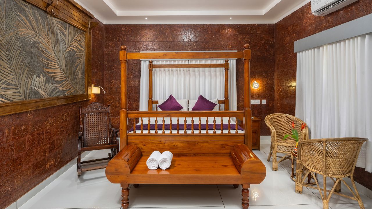 A four-poster bed with a wooden frame, two purple pillows, and rolled towels on the footboard.