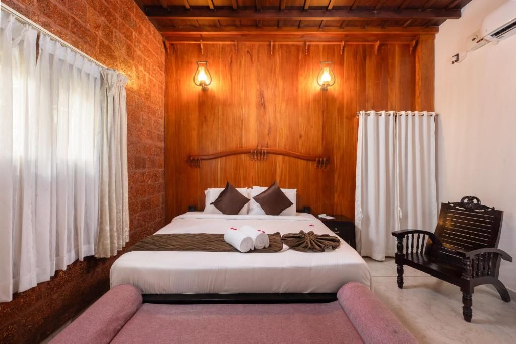 Habitación de hotel con pared de ladrillo, techo de madera, cama con almohadas, un banco y una mesita de noche.