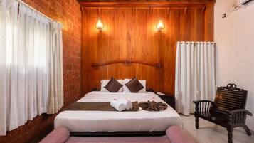 Habitación de hotel con pared de ladrillo, techo de madera, cama con almohadas, un banco y una mesita de noche.