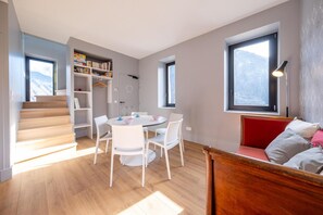 Um interior moderno com uma mesa de jantar redonda, cadeiras brancas, uma estante, uma escadaria e um sofá vermelho.