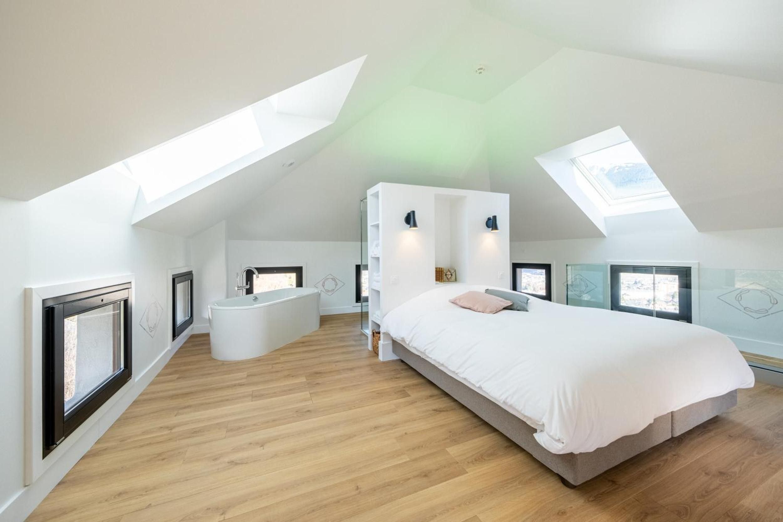 Une chambre à coucher moderne dotée d’une lucarne, d’un grand lit, d’une baignoire intégrée et d’une cabine de douche en verre.