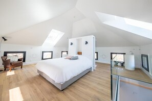 Um quarto espaçoso com uma cama grande, uma cadeira e varanda envidraçada.