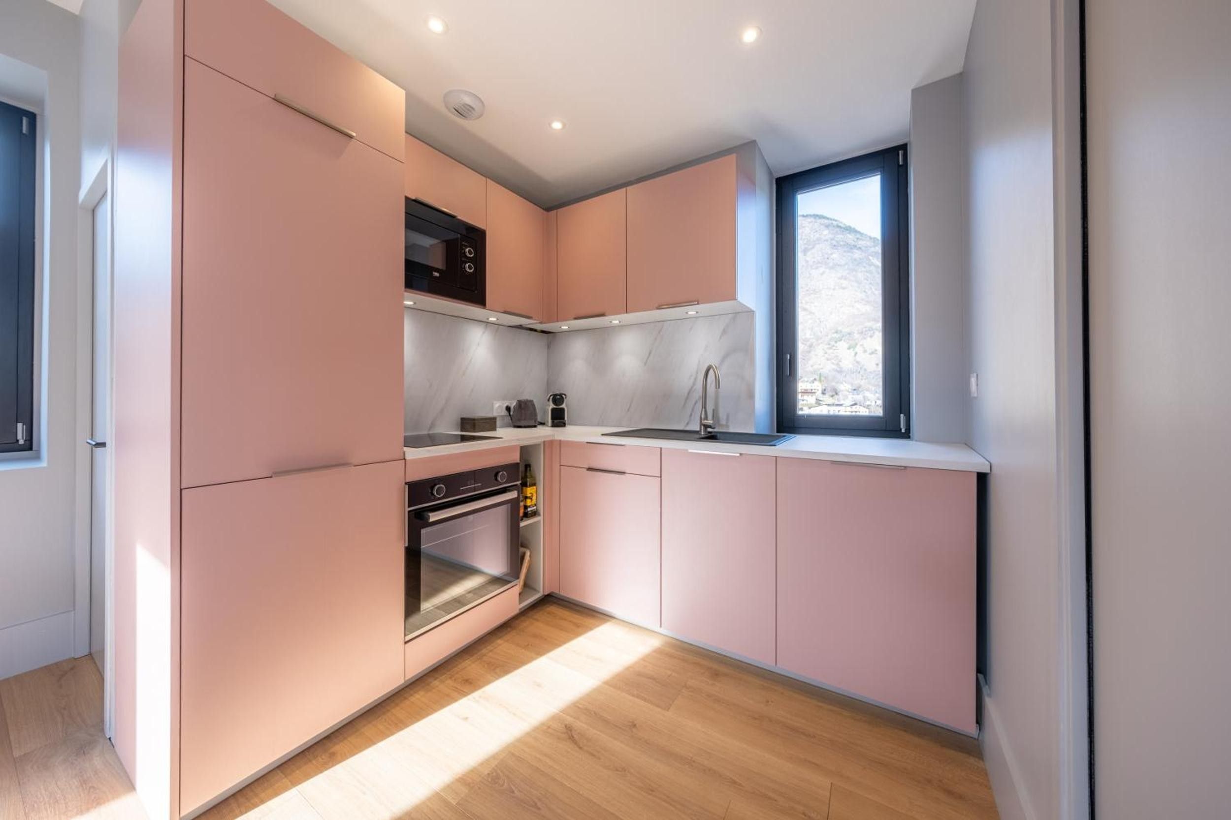 Eine moderne Küche mit rosa Schränken, einem eingebauten Ofen und einem Fenster mit Blick.