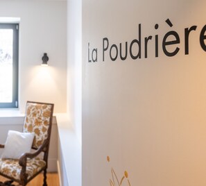 Una habitación con una silla y una pared con el texto 'La Poudriere'.