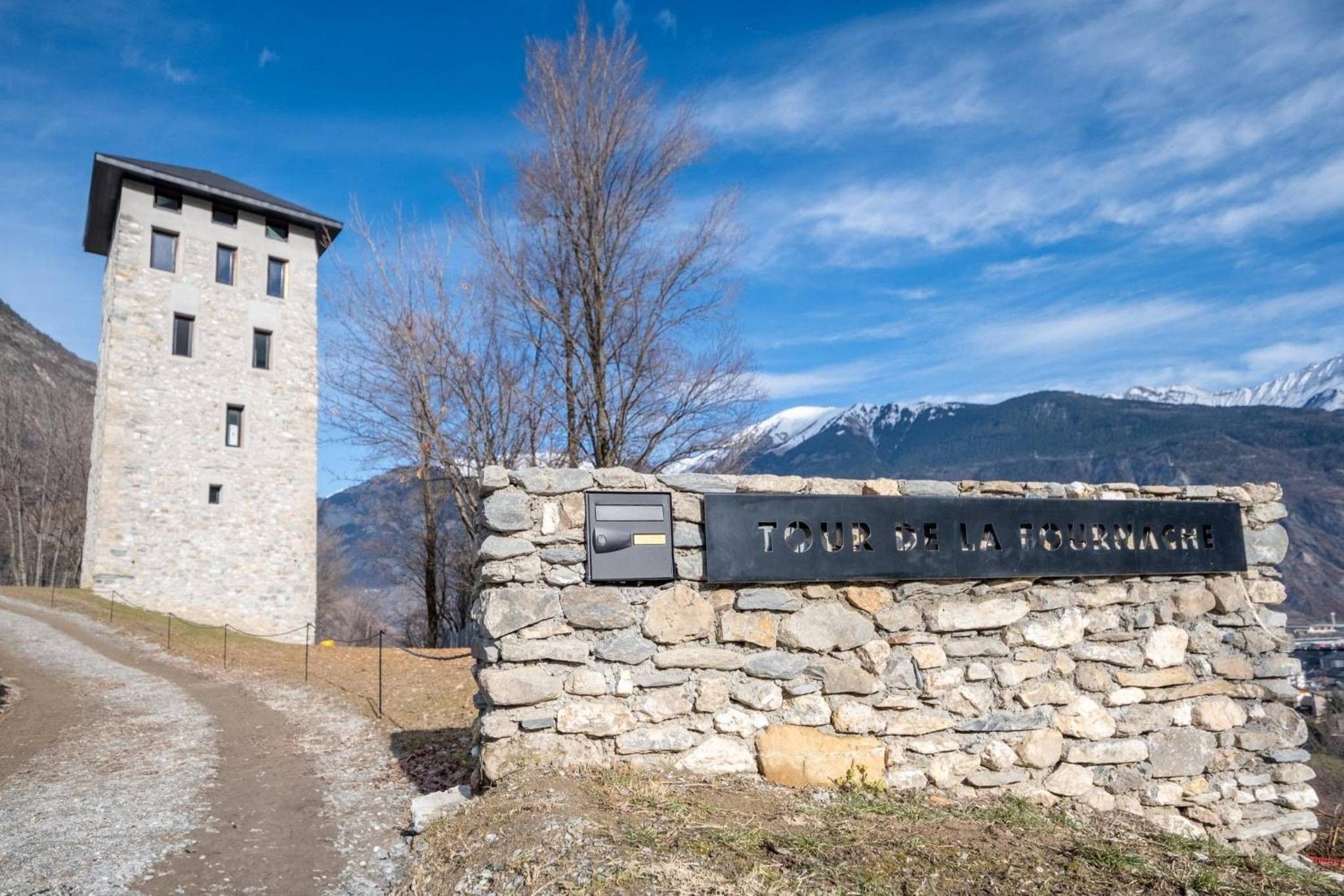 Un mur de pierre sur lequel est apposée une plaque indiquant « TOUR DE LA FISCHMACHER », et un bâtiment en pierre doté d’un toit plat.