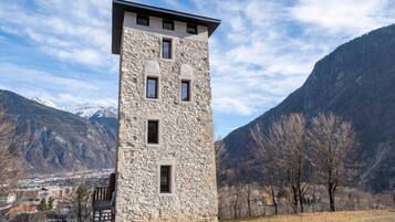 Ein steinerner Turm mit zahlreichen Fenstern vor einer Bergkulisse.