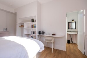 Une chambre à coucher avec un lit, un bureau blanc avec des étagères, une chaise et une salle de bain avec un lavabo et un miroir.