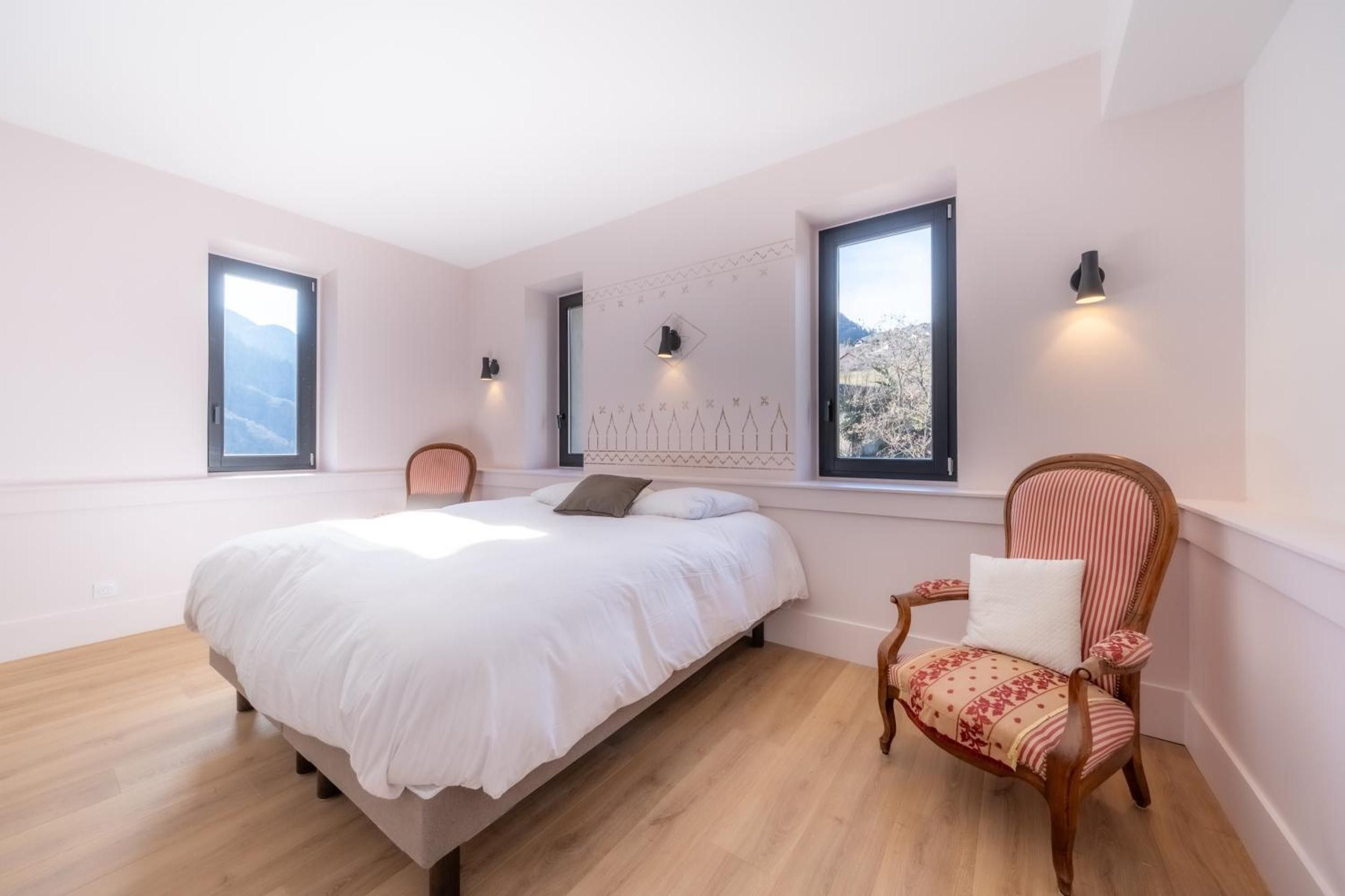 Une chambre à coucher avec un lit, une chaise et deux fenêtres équipées de lampes fixées au mur.