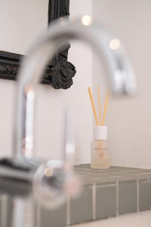 Un lavamanos de baño con un grifo moderno y un difusor de cañas marca Escape.