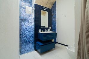Ein Badezimmer mit blauer Mosaikfliesenwand, einem weißen Waschbecken und einem Spiegel darüber.
