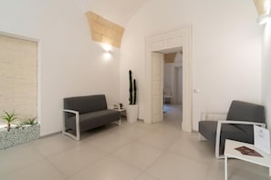 A modern living room with a grey sofa, a white armchair, and a cactus plant. - Apartment 'Calcarìa Suite - 2' with Shared Terrace, Wi-Fi and Air Conditioning (Lecce)