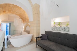 Ein modernes Badezimmer mit einer freistehenden Badewanne, einem grauen Sofa und einer Wandpflanze mit Pflanzen.