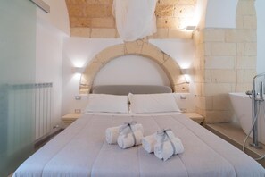 Ein Hotelzimmer mit einer Wand aus Stein, einem Bett mit weißer Bettwäsche, zwei Nachttischen und einem Badezimmer mit einer Badewanne.