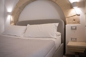 Ein Bett mit weißer Bettwäsche, eine Wand aus Stein und Wandleuchten.