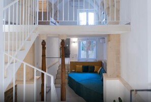 Een slaapkamer met een bed, een raam en een trap naar een hoger gelegen verdieping.