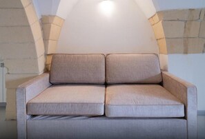 A beige sofa with a cushioned backrest and armrests, positioned against a wall with a recessed lighting fixture above. - Apartment 'Calcarìa Suite - 3' with Shared Terrace, Wi-Fi and Air Conditioning (Lecce)