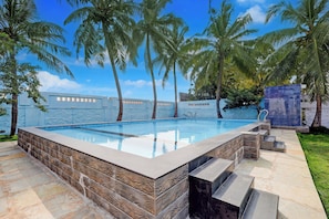 A rectangular swimming pool with stone-textured walls, surrounded by palm trees and a clear blue sky. - Palette RC Resort  Kovalam Beach ECR (Chennai)
