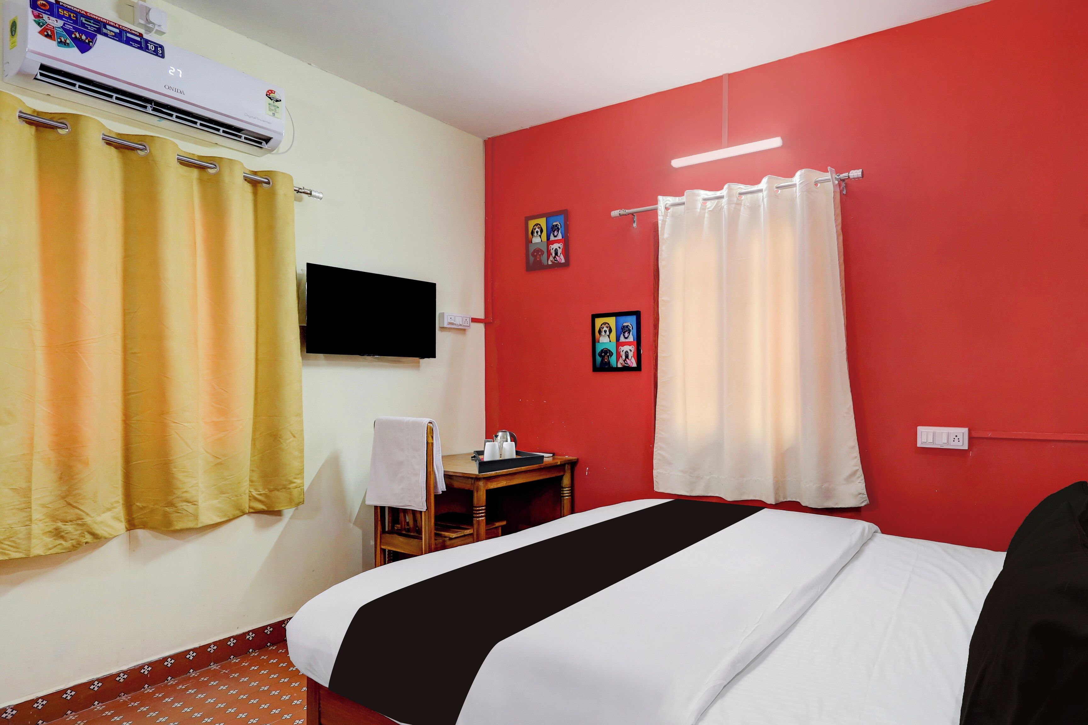 A hotel room with a bed, a small table, a chair, a TV, and a wall-mounted air conditioner.