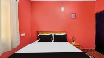 Una habitación con una cama, una mesita de noche, un reloj de pared y una ventana con cortinas.