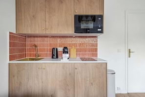 A compact kitchen with wooden cabinets, a built-in microwave, a kettle, and a coffee machine. - Charming Paris Apartment on Rue de Vaugirard (Paris)