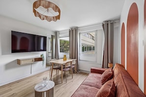 A modern living room with a flat-screen TV, a dining table with chairs, a sofa, and a small side table. - Charming Paris Apartment on Rue de Vaugirard (Paris)