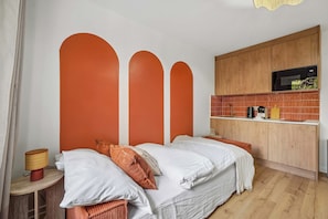 A bedroom with a bed, a bedside table, a lamp, and a kitchen area with a microwave. - Charming Paris Apartment on Rue de Vaugirard (Paris)