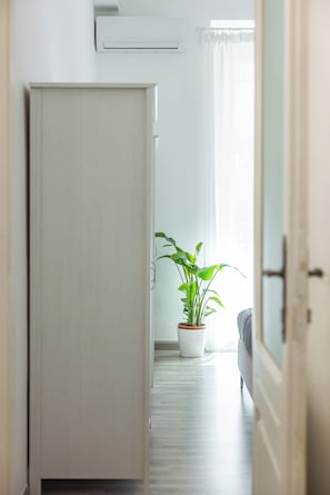 Um corredor com porta fechada, planta em vaso e cama ao fundo.