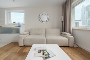 Un salon moderne avec un canapé, une table basse sur laquelle sont posés des magazines, un miroir fixé au mur et une fenêtre avec des rideaux.