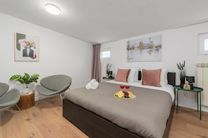 A modern hotel room with a large bed, a seating area with a chair, a small table, and a potted plant. - Lumina 3 room Apart near Pałac Kultury (Warszawa)