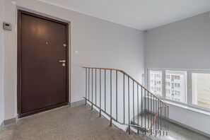A staircase with a metal railing, a brown door, and a window overlooking a building. - Lumina 3 room Apart near Pałac Kultury (Warszawa)